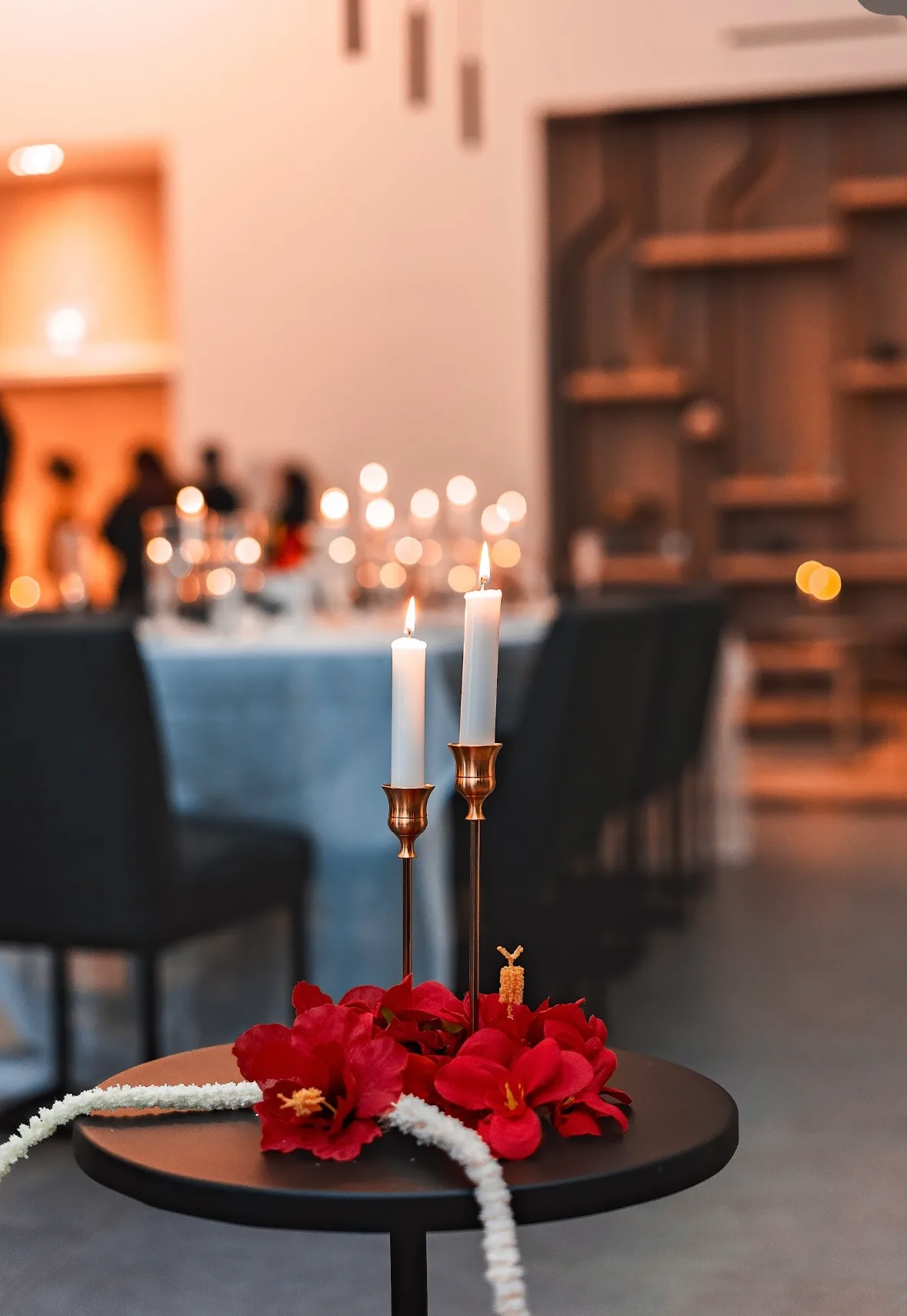 Red flowers and taper candles glowing beside a dinner table